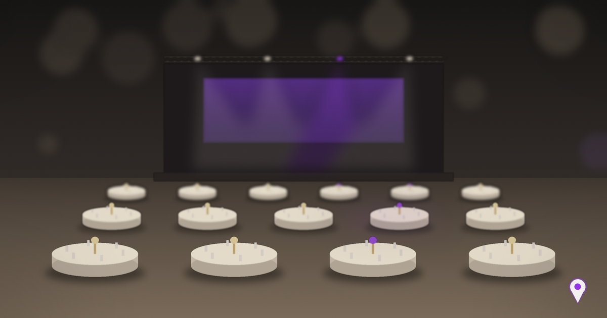 Salão de eventos corporativos com mesas redondas postas em primeiro plano e palco ao fundo iluminado por refletores, com tela em tom roxo